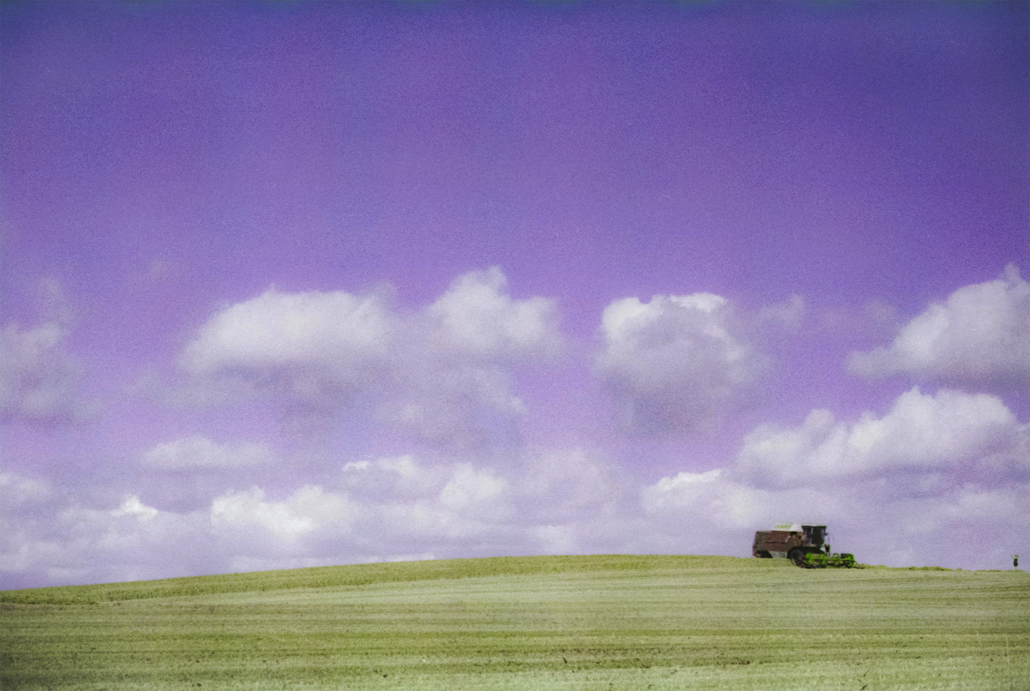 Bucolicism — peak summer farmland in southern Sweden with a modern combine harvester atop a hill, shot on color-shift film.