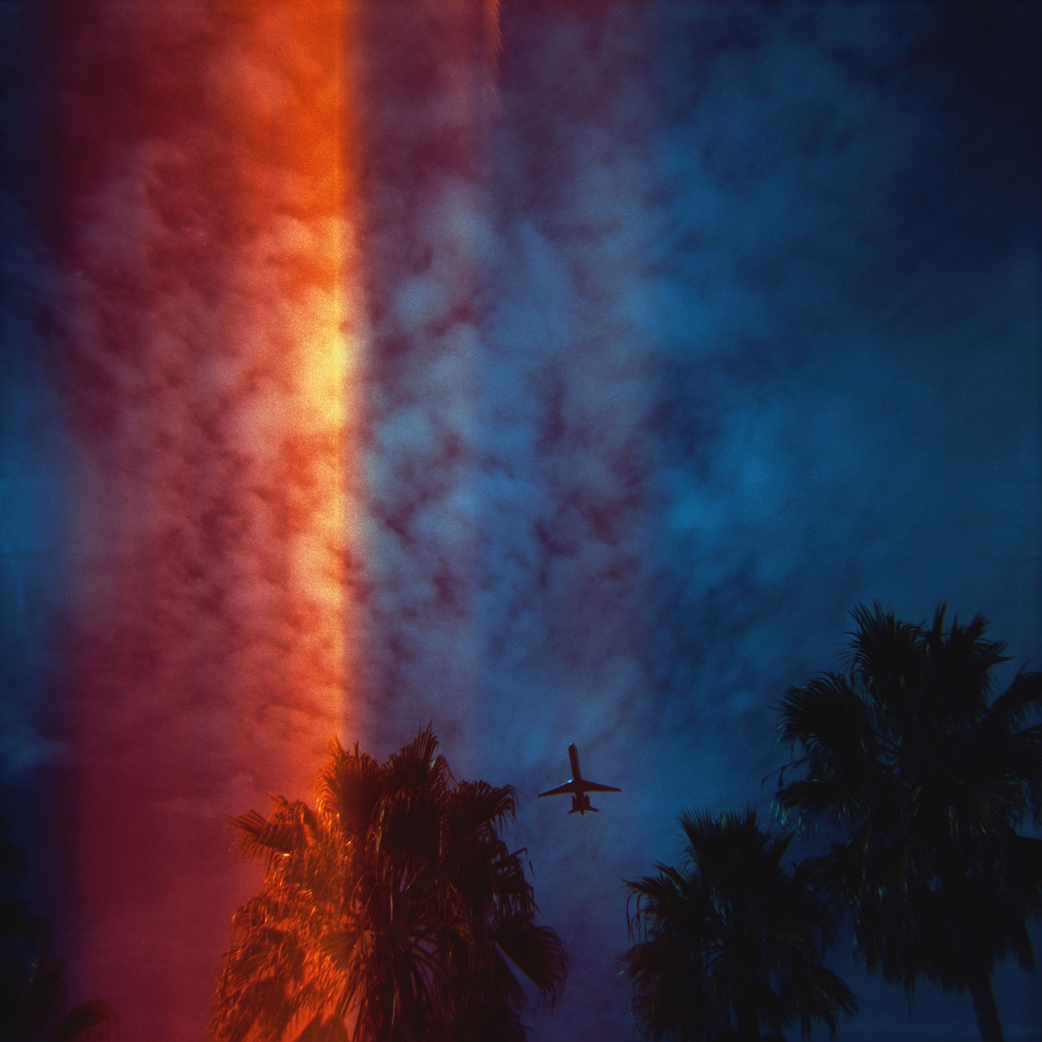 La Nuit Américaine — a plane taking off low over LAX with light-leaked shafts of color falling on palm trees, day-for-night style.